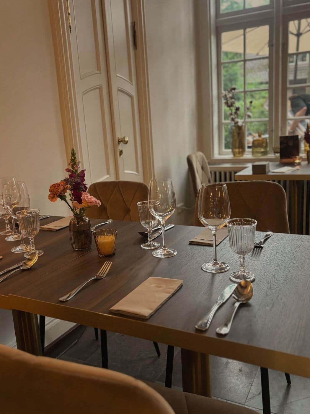 Gedeckter Tisch mit Weingläsern, Serviette und Blumen vor einer hellen Kassettentür